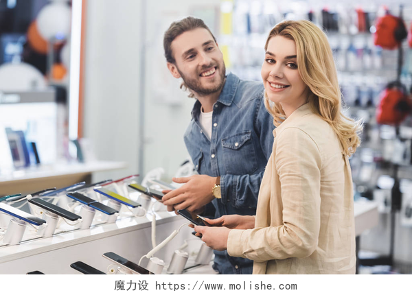 一对情侣正在商场里选购智能手机微笑的男女朋友在家用电器商店里拿着新的智能手机 